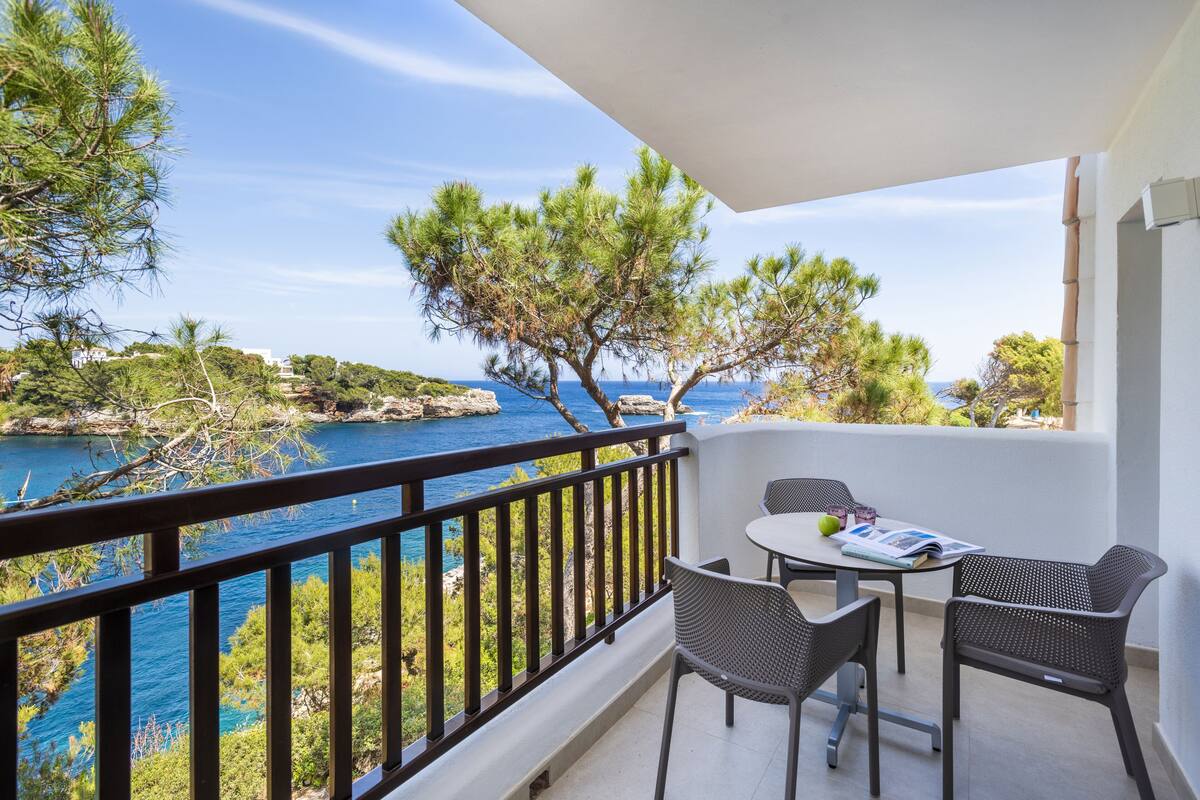 A balcony with a view of the sea, featuring a table with chairs and a magazine.