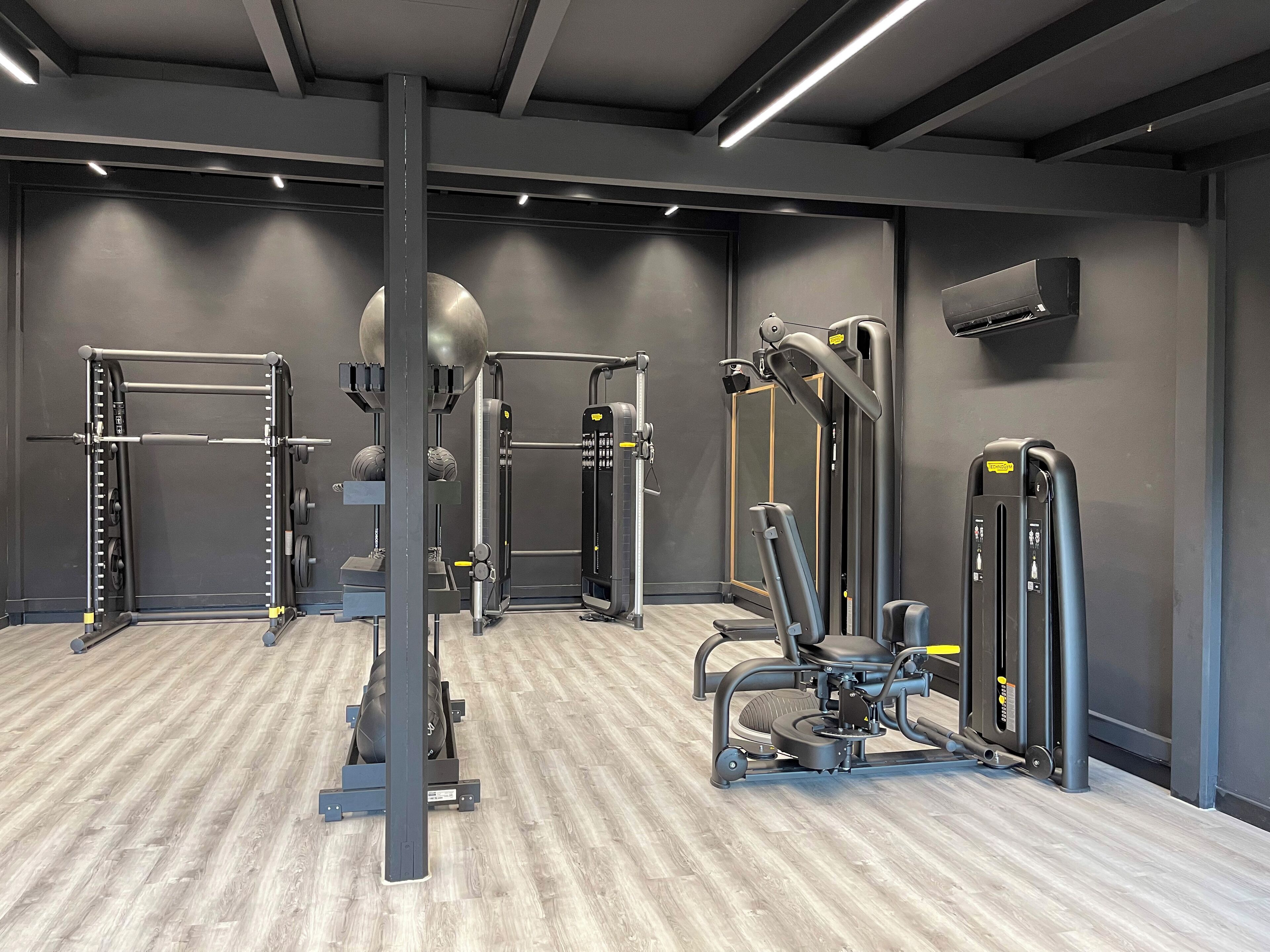 Une salle de sport moderne équipée de divers appareils d’entraînement, notamment un support à squat, une machine à câbles et un banc de musculation.