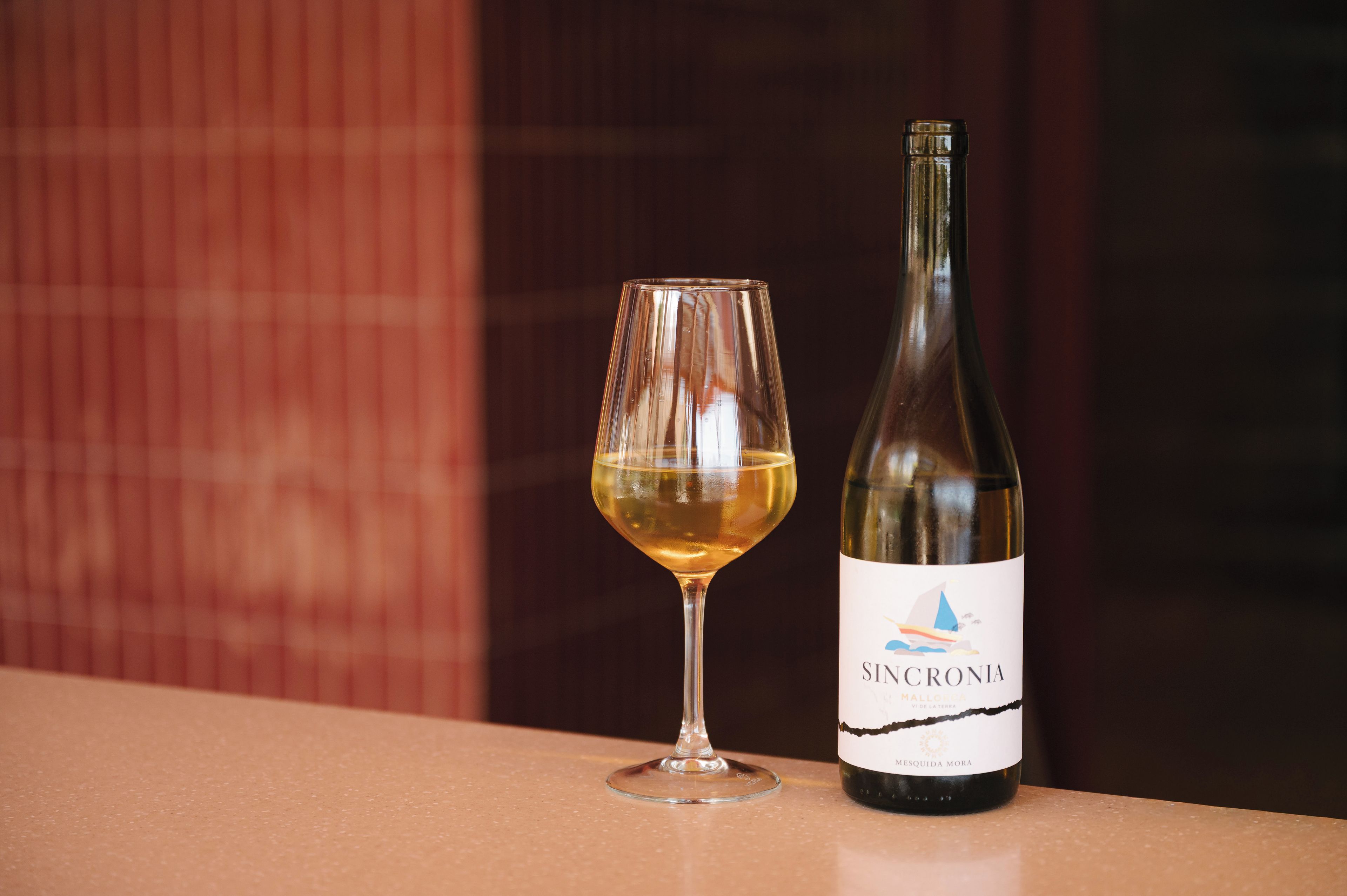 A wine glass and a bottle of Sincronia wine on a countertop.