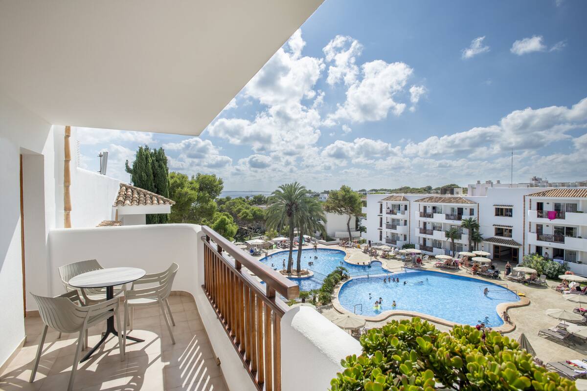A balcony with a view of a swimming pool complex, including multiple pools and lounge areas.