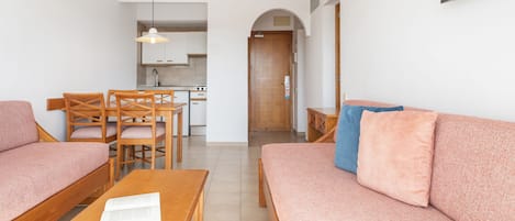 Ein modernes Wohnzimmer mit einer Couch, Sesseln, einem Couchtisch und einem an der Wand befestigten Fernseher.