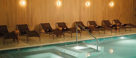A swimming pool with lounge chairs and steps leading into the water.
