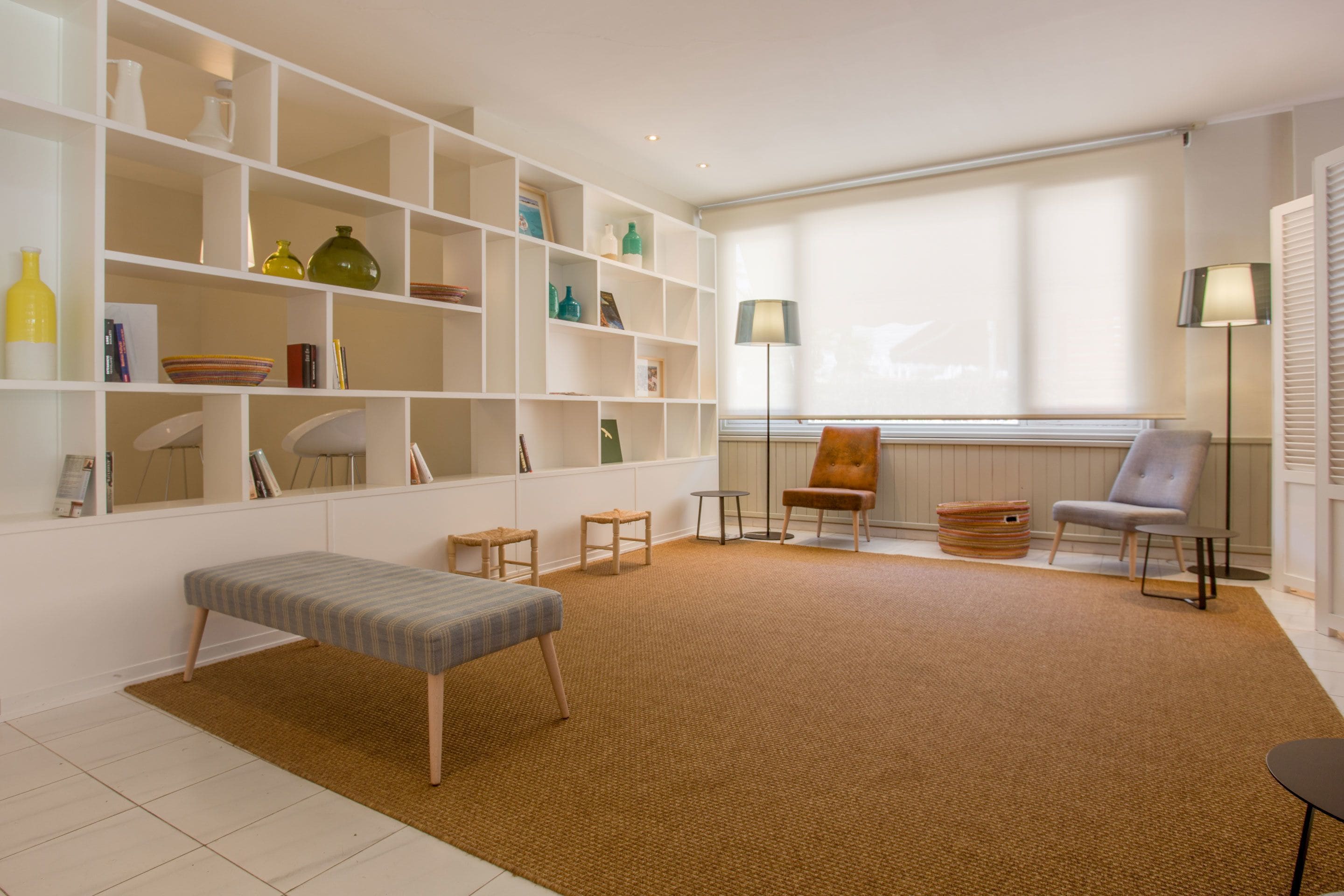 Una sala de estar moderna con un banco, estanterías decoradas, una silla y una lámpara de pie.