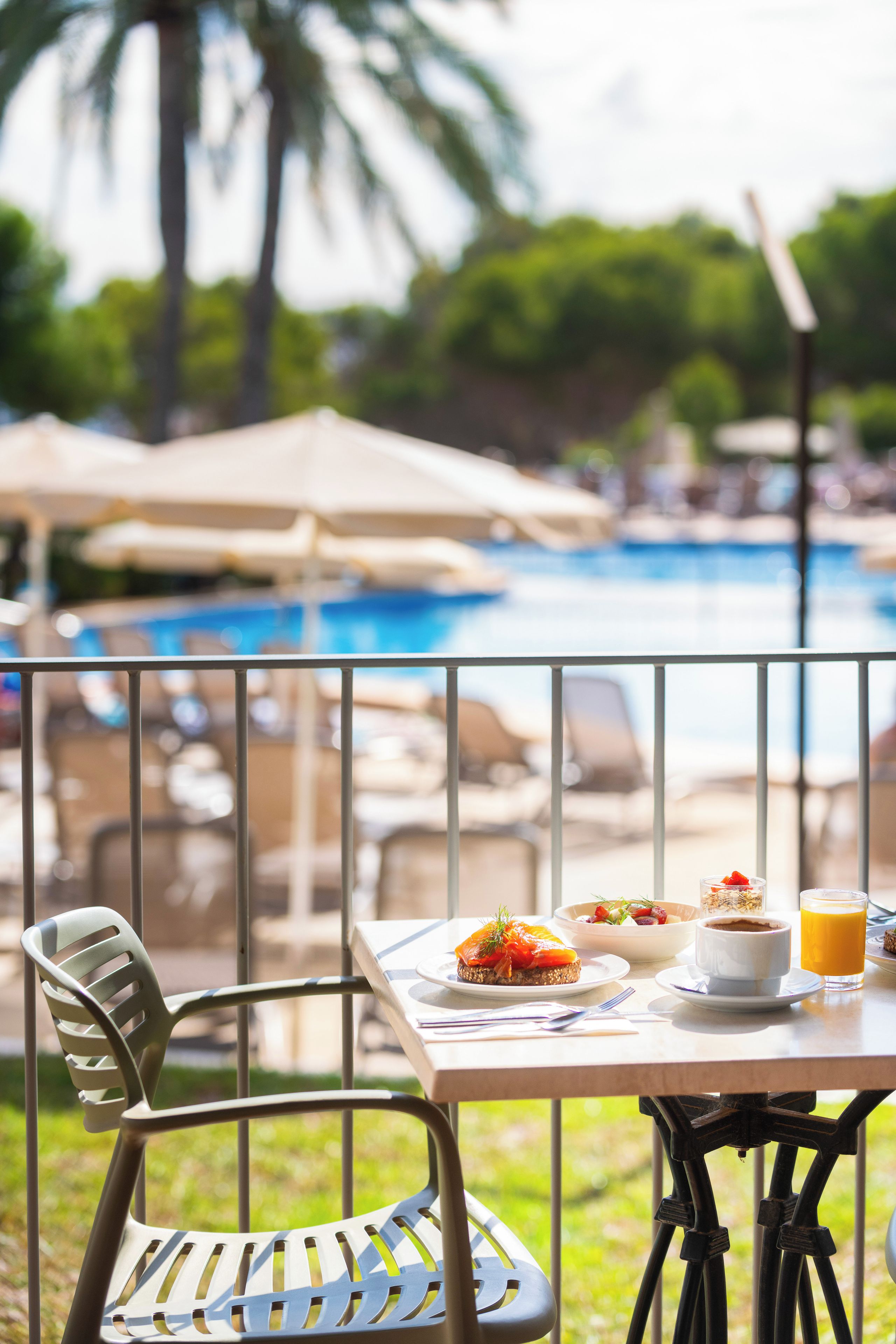 A dining table with a meal, a glass of orange juice, and a view of a swimming pool.
