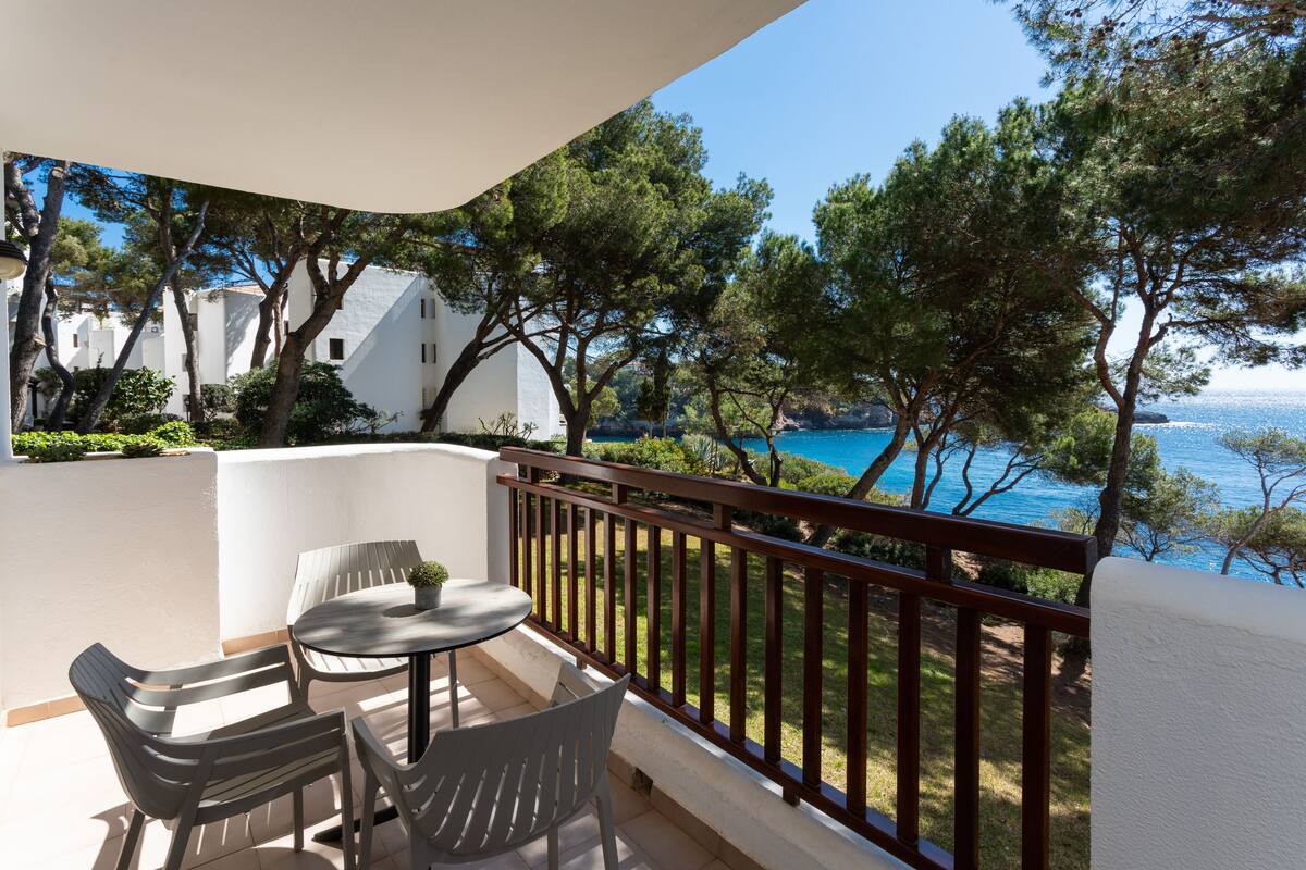 A balcony with a view of the sea, a table with chairs, and a potted plant.