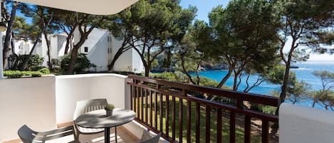 A balcony with a view of the sea, a table with chairs, and a potted plant.