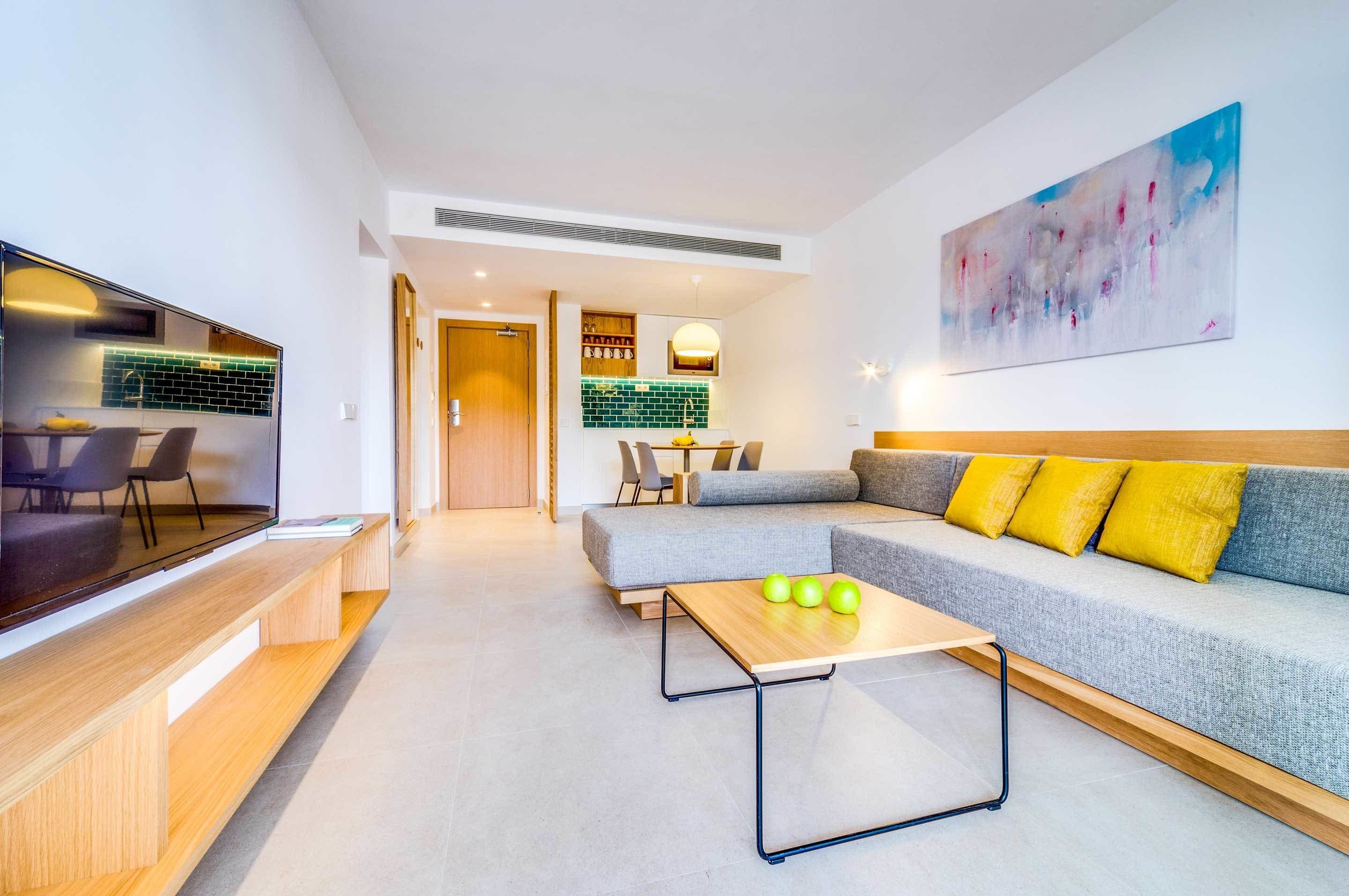 A modern living room with a grey sofa, yellow cushions, a wooden coffee table, and a flat-screen TV.