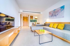 Uma sala de estar moderna com um sofá cinzento, almofadas amarelas, uma mesa de centro de madeira e uma televisão de tela plana.