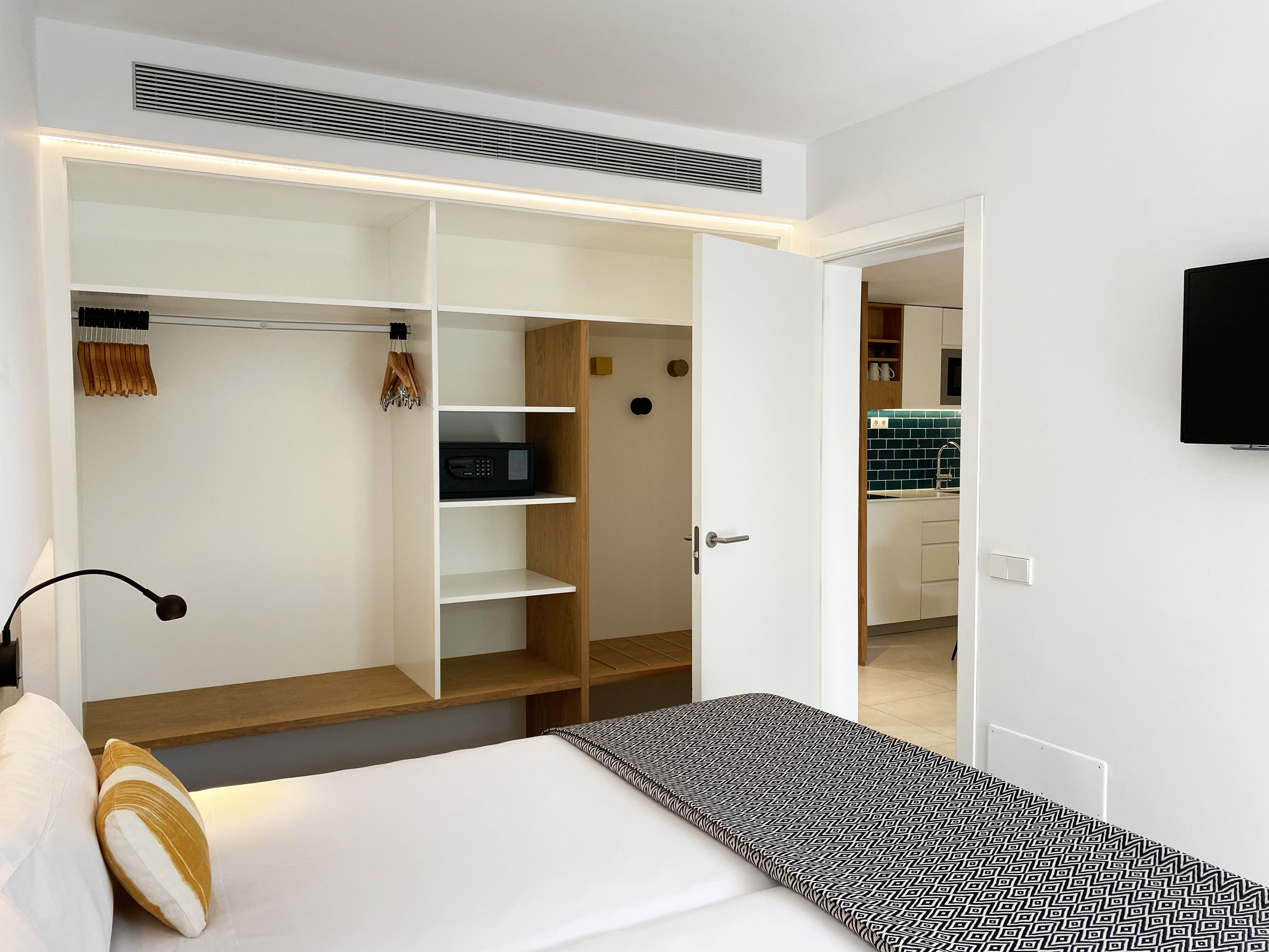 A modern hotel room with a bed, bedside table, and a walk-in closet with shelves and a hanging rack.