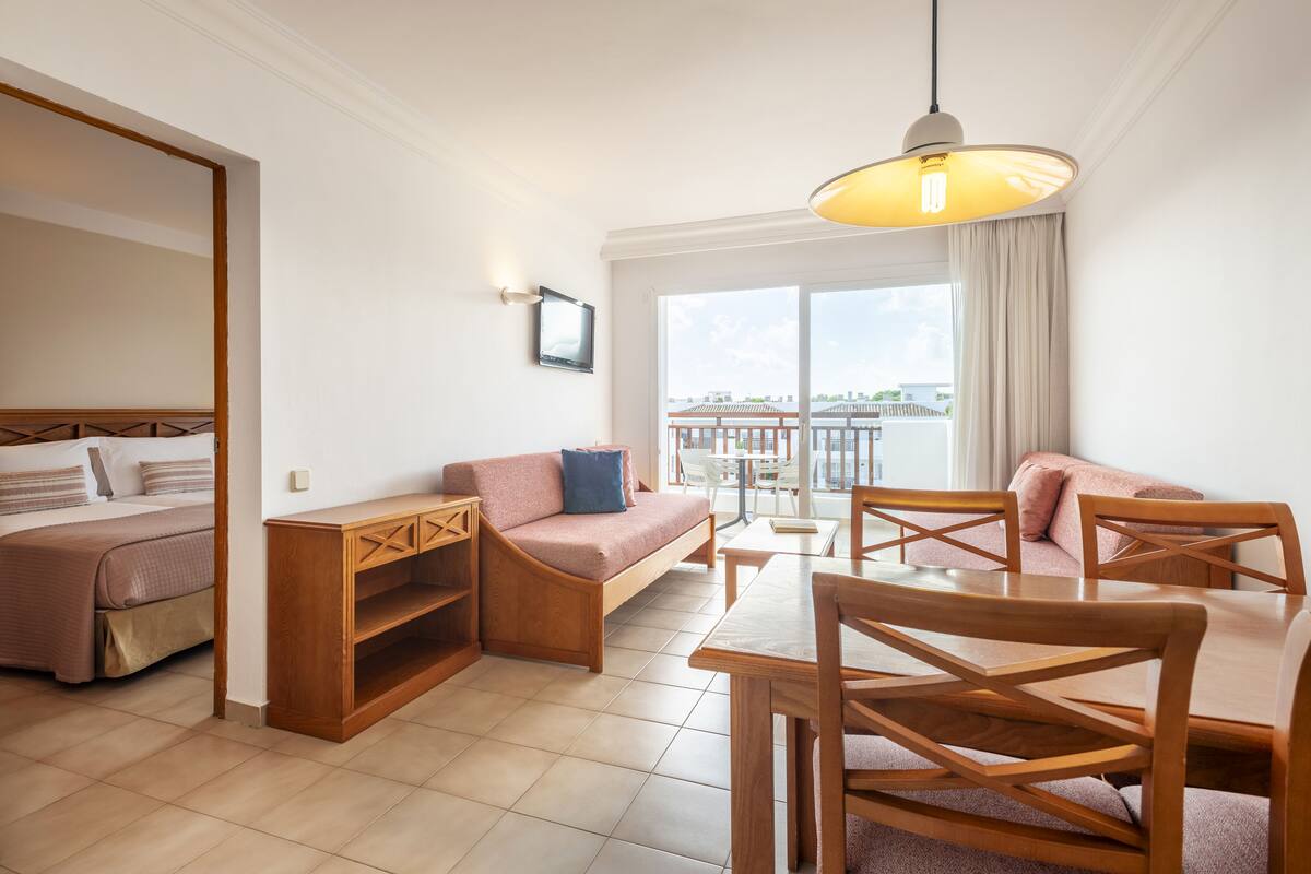 A modern hotel room with a bed, a sofa, a dining table, and a balcony with a view.