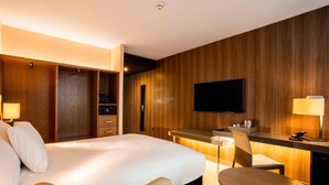 A hotel room with a large bed, a desk, a chair, a television, and a minibar. - AC Hotel by Marriott, Manchester Salford Quays (Salford)