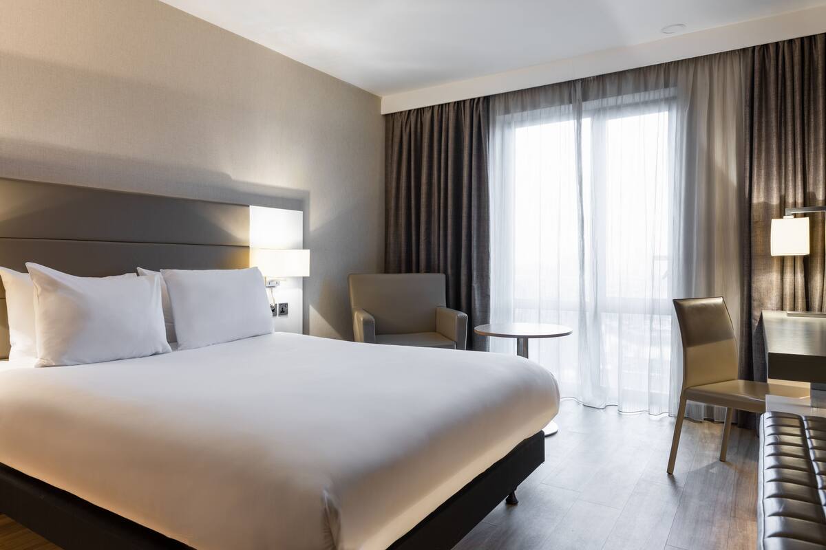 A hotel room with a large bed, a chair, a small table, and a desk.
