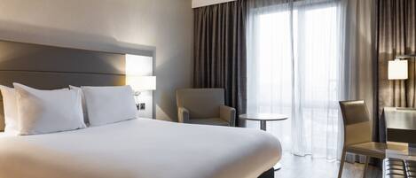 Une chambre d’hôtel avec un grand lit, une chaise, une petite table et un bureau.
