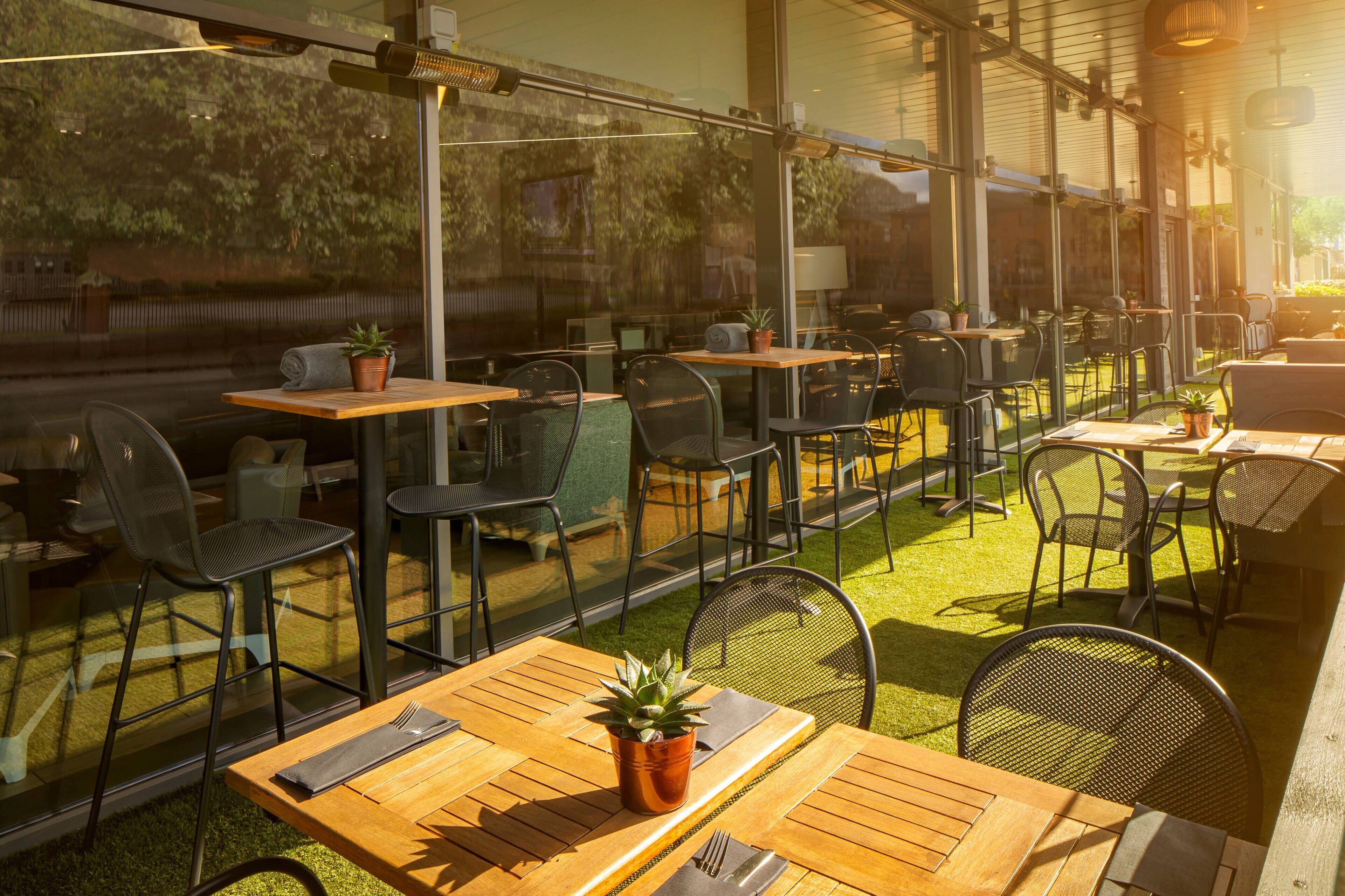 Un café al aire libre con mesas y sillas de madera, plantas en macetas y vistas al follaje circundante.