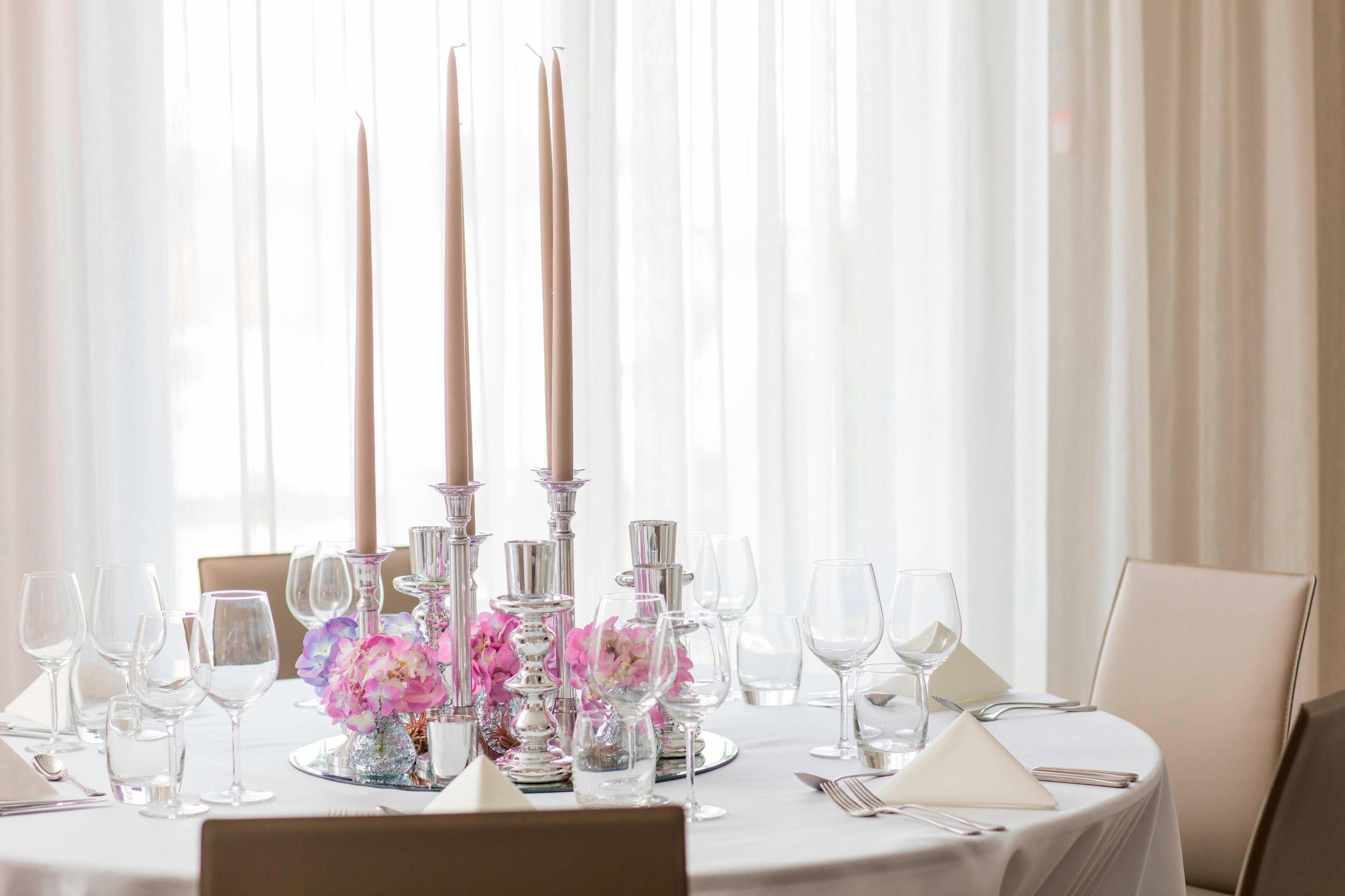 A table set for a formal dining occasion with clear glassware, silver candelabras, and pink flowers.