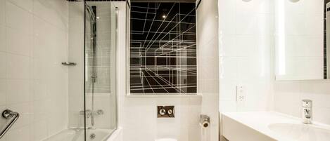 Ένα σύγχρονο μπάνιο με ένα ντους που διαχωρίζεται με γυάλινο διαχωριστικό, μια λευκή τουαλέτα και έναν νιπτήρα με έναν καθρέφτη ακριβώς από πάνω.
