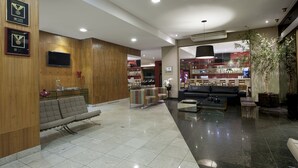 A modern hotel lobby with a reception desk, seating area, and a bar.