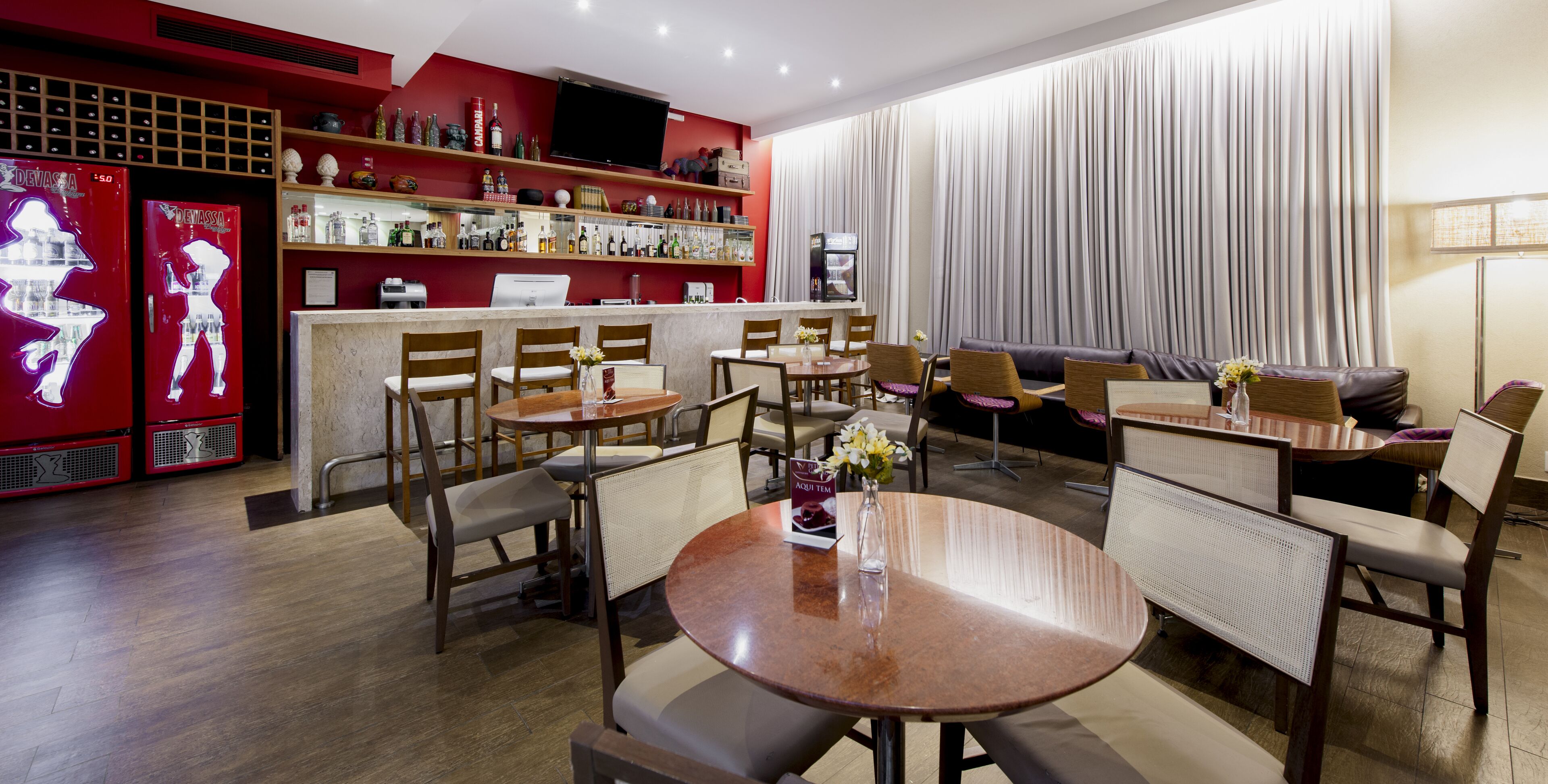 Un moderno vestíbulo de hotel con zona de bar, arreglos de asientos y un gran ventanal con cortinas.