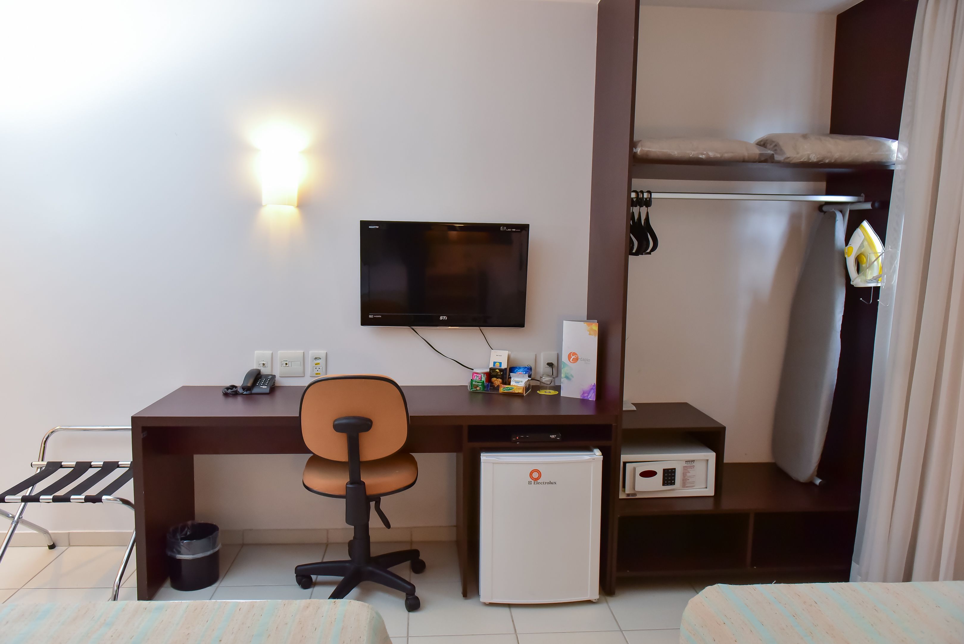 A compact hotel room with a desk, chair, television, mini-fridge, and a bed.