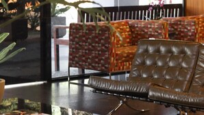 A lobby with a leather sofa, patterned cushions, a glass coffee table, and a large plant.