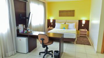 A hotel room with a bed, desk, chair, and a small refrigerator.