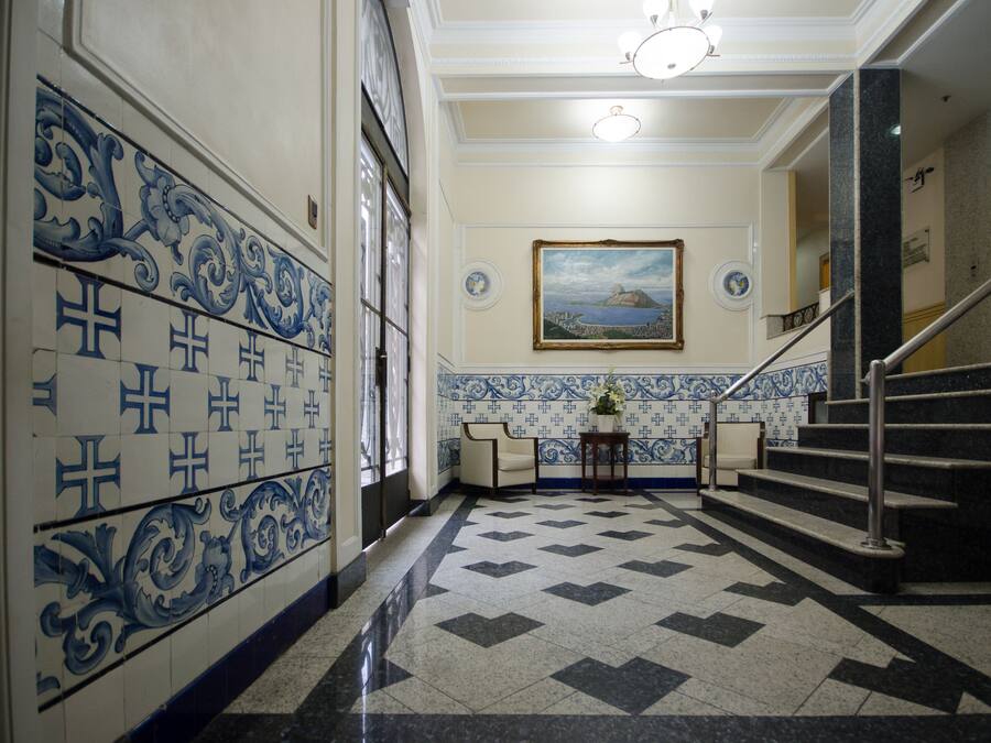 Um corredor com azulejos estampados, uma escada e um quadro pendurado na parede.