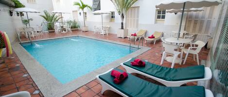 A swimming pool with lounge chairs and umbrellas, surrounded by potted plants and a tiled patio.