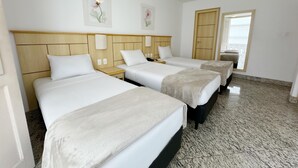 Une chambre d’hôtel avec trois lits, une tête de lit en bois, une porte et une fenêtre.