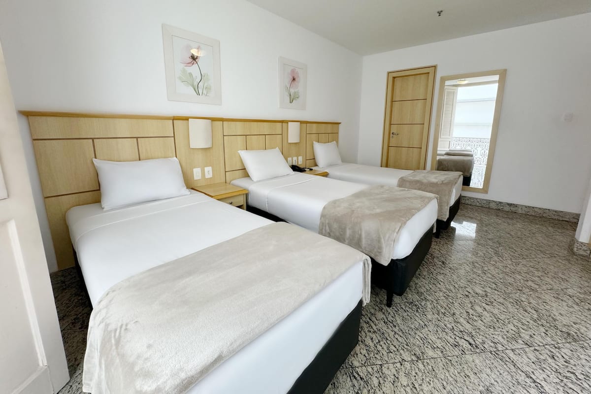 Ein Hotelzimmer mit drei Betten, einem Holzkopfteil, einer Tür und einem Fenster.