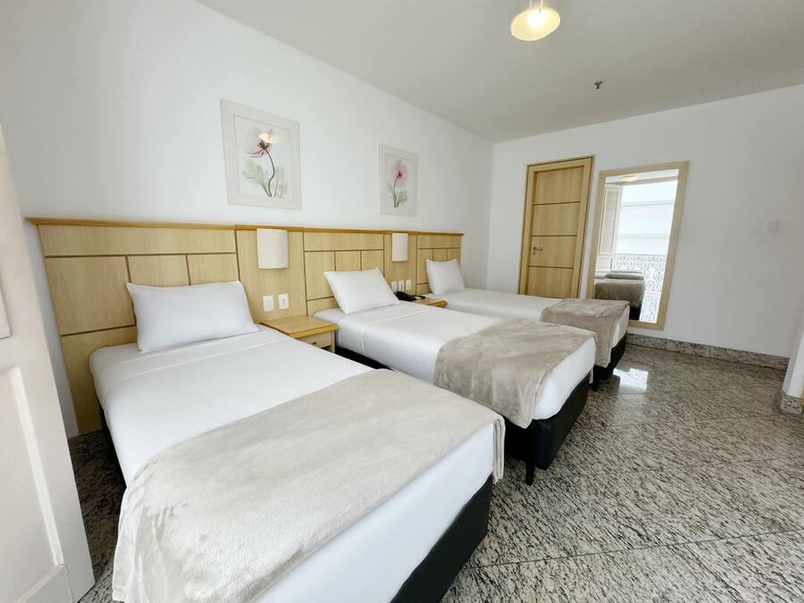 Habitación de hotel con tres camas, cabecera de madera, una puerta y una ventana.