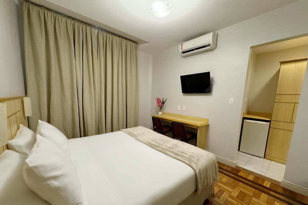 Ein Hotelzimmer mit Bett, Schreibtisch, Fernseher, Klimaanlage und Minikühlschrank.
