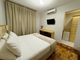 Habitación de hotel con cama, escritorio, televisor, aire acondicionado y un refrigerador pequeño.