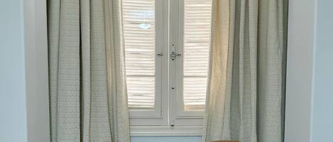 Una habitación con dos sillones de cuero marrón, una ventana con contraventanas blancas y un suelo de parqué de madera.