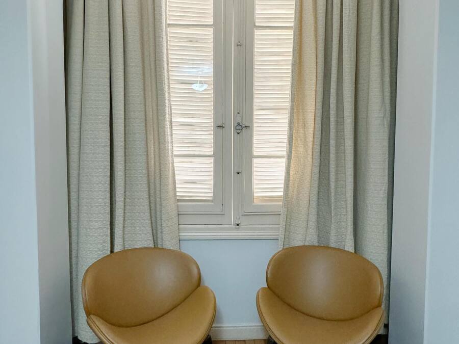 Una habitación con dos sillones de cuero marrón, una ventana con contraventanas blancas y un suelo de parqué de madera.