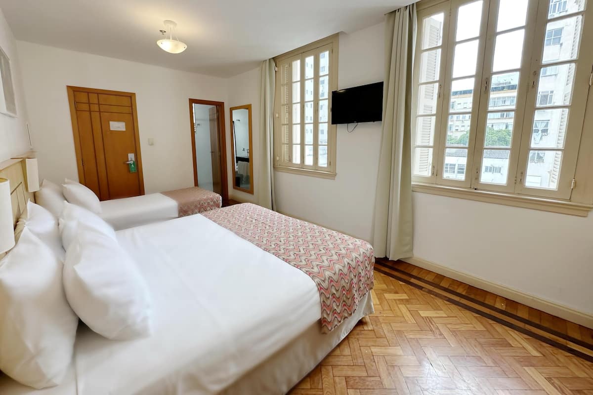 Ein Hotelzimmer mit zwei Betten, einem Fernseher, großen Fenstern und Holzboden.