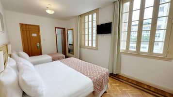 A hotel room with two beds, a TV, large windows, and a wooden floor.