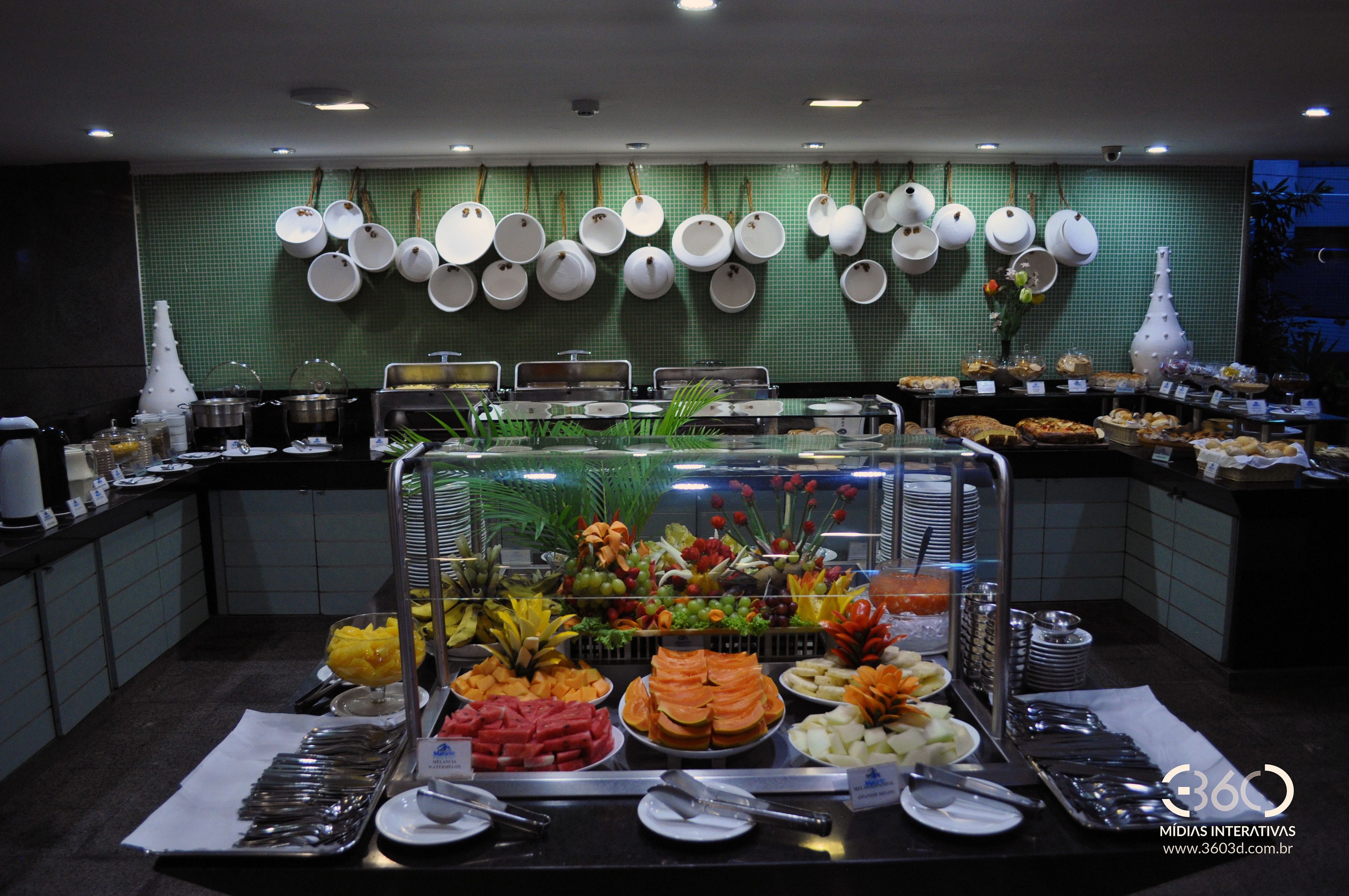 A buffet with various food items and utensils, a green tiled wall, and hanging dishes.