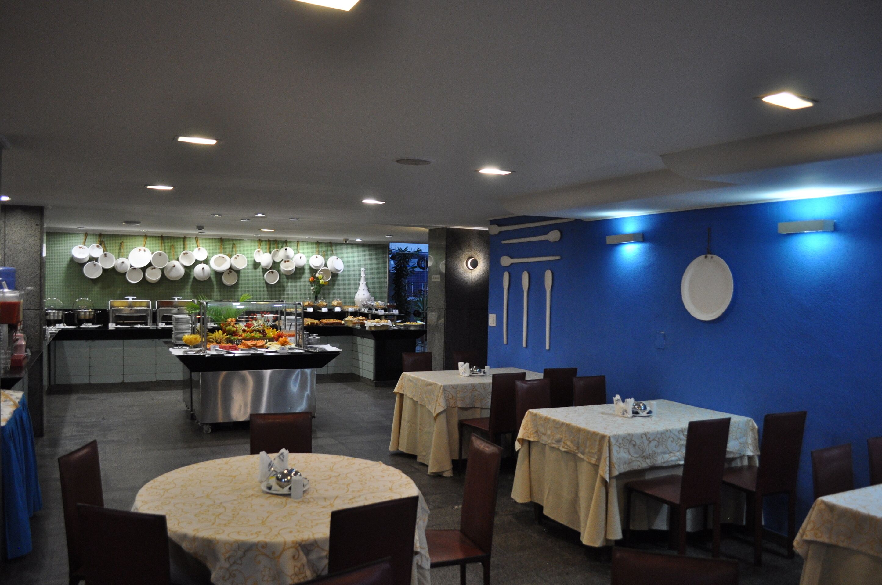 Ein Restaurant mit runden Tischen und Stühlen, einem Buffetbereich und einer blauen Wand mit einer Uhr.