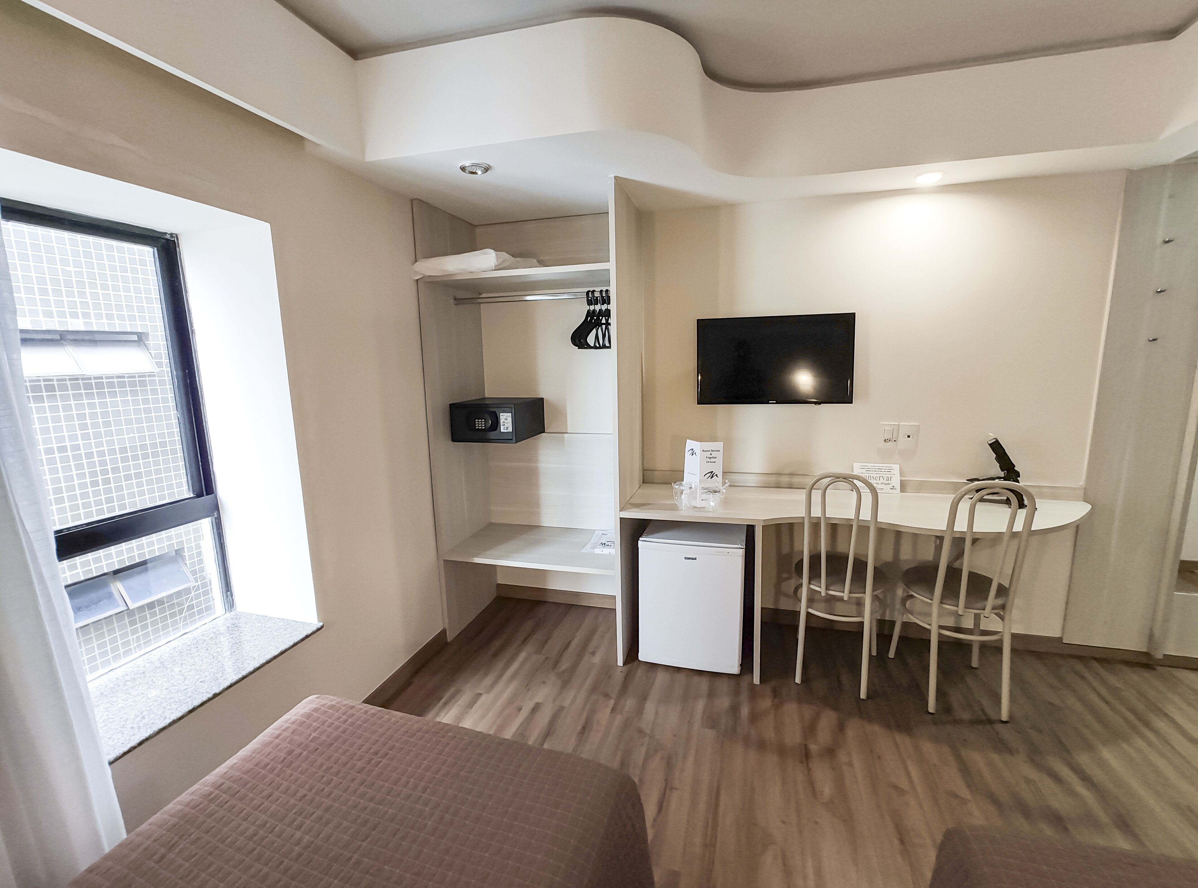 Una habitación compacta con kitchenette, un comedor con mesa y sillas, un refrigerador pequeño, un microondas y un televisor montado en la pared.