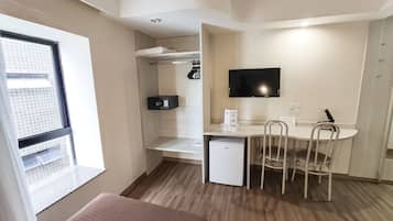 Una habitación compacta con kitchenette, un comedor con mesa y sillas, un refrigerador pequeño, un microondas y un televisor montado en la pared.