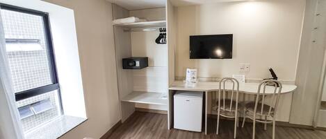 A compact room with a kitchenette, a dining area with a table and chairs, a small refrigerator, a microwave, and a TV mounted on the wall.