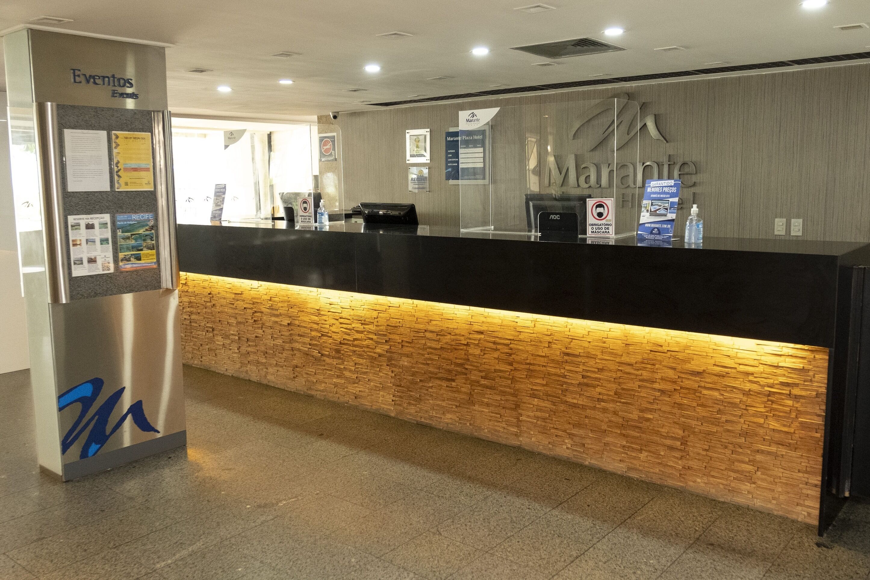 A hotel reception desk with a wooden accent wall, a digital screen, and a sign for the Marante Hotel.
