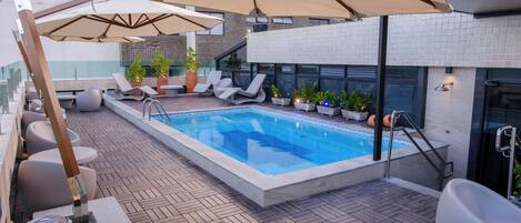 Ett poolområde på taket med solstolar, parasoller och en modern arkitektonisk design.