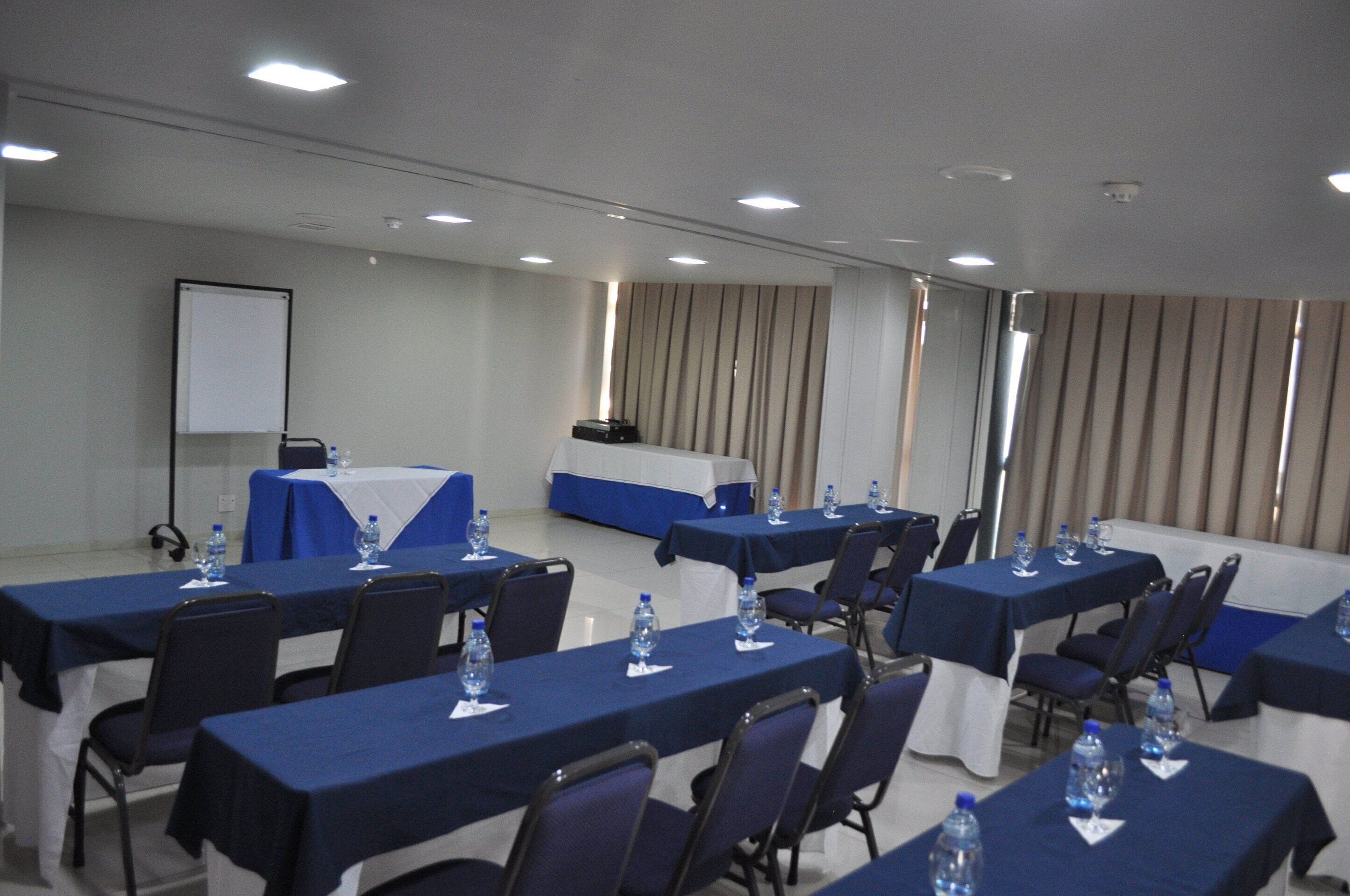 Un salón de conferencias con varias mesas, sillas y botellas de agua.