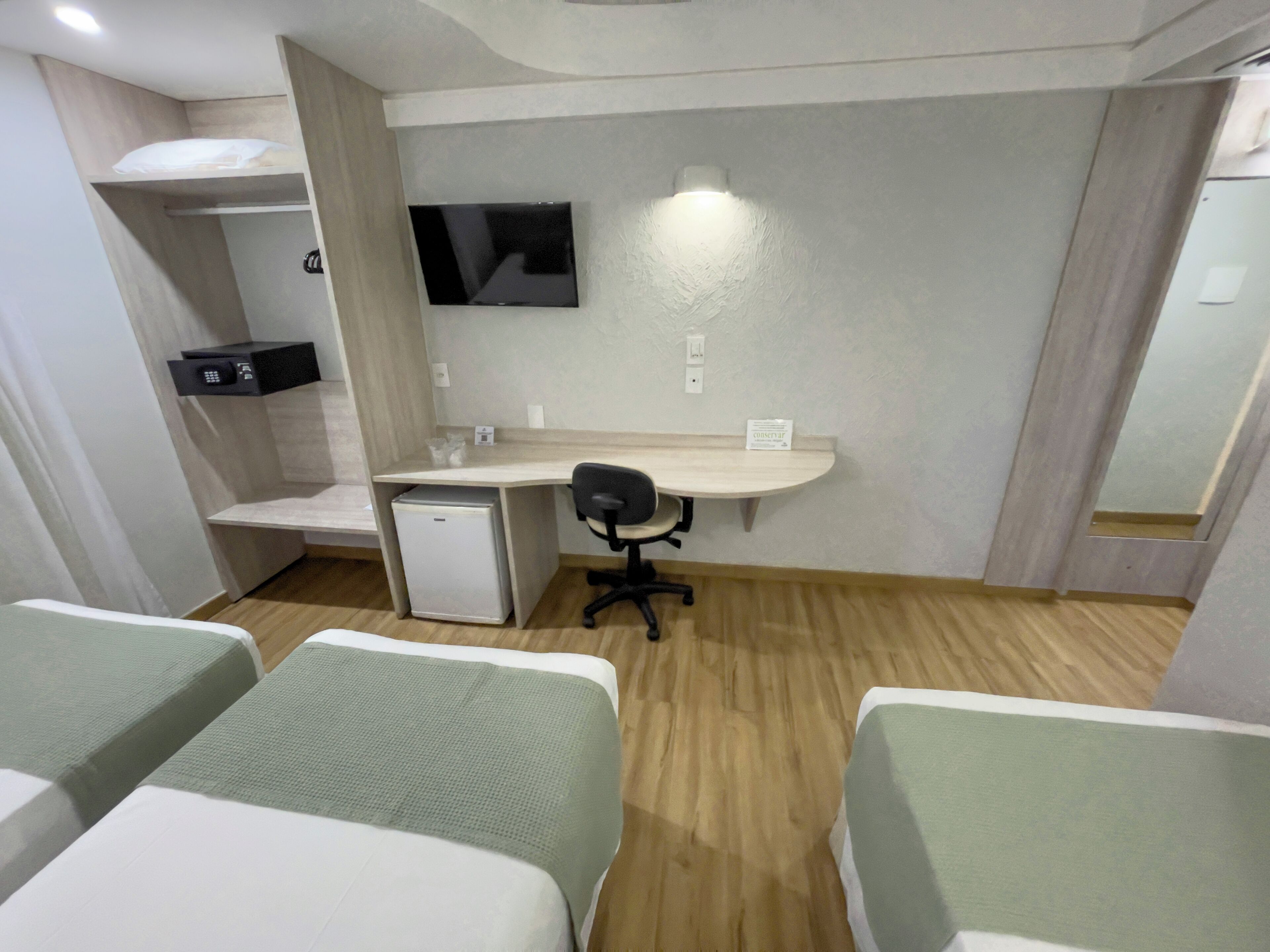 Una habitación de hotel con cama, escritorio, silla, televisor y un refrigerador pequeño.