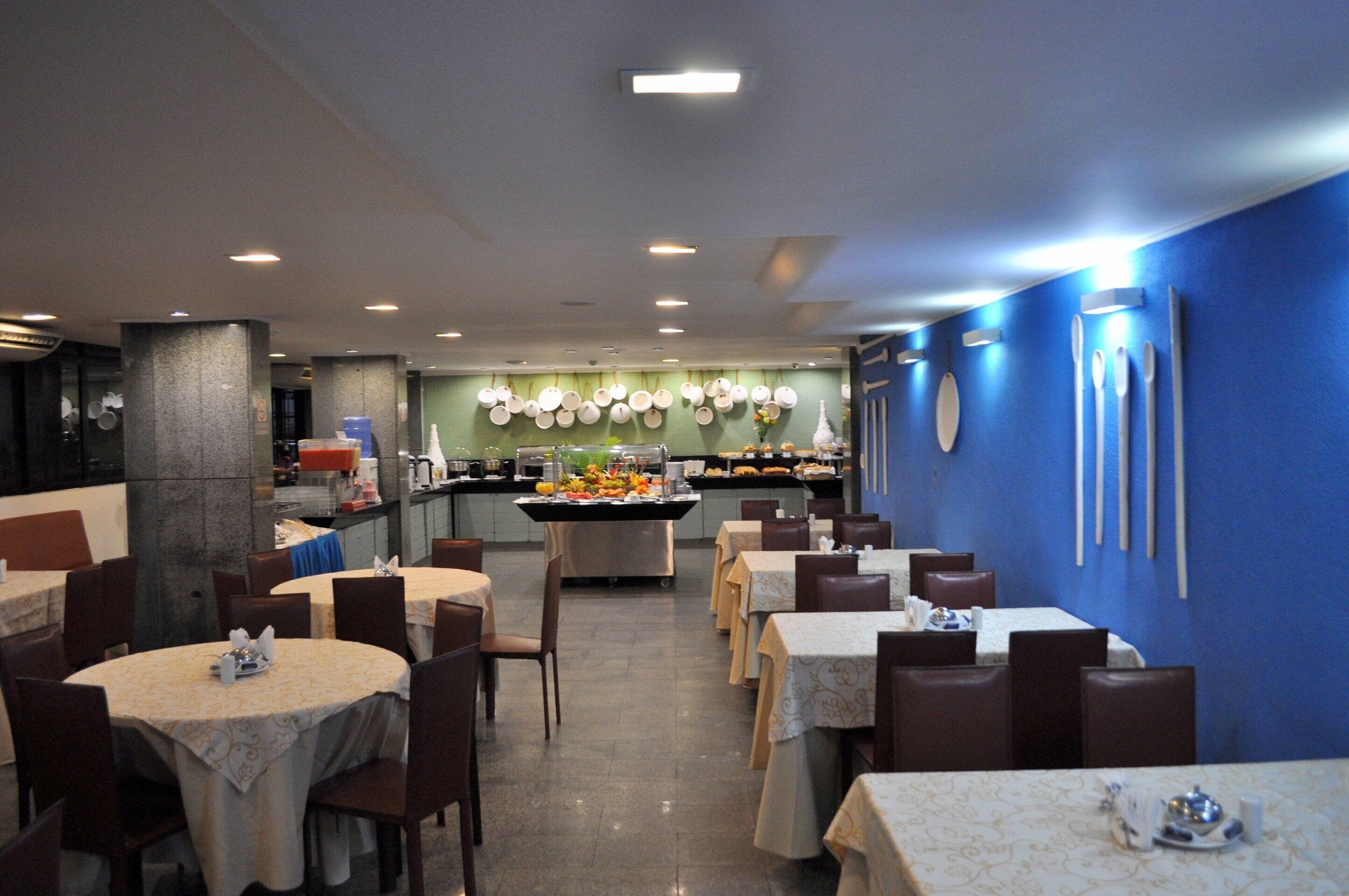 Un restaurante con mesas y sillas redondas, una zona de buffet central y una pared de acento azul.