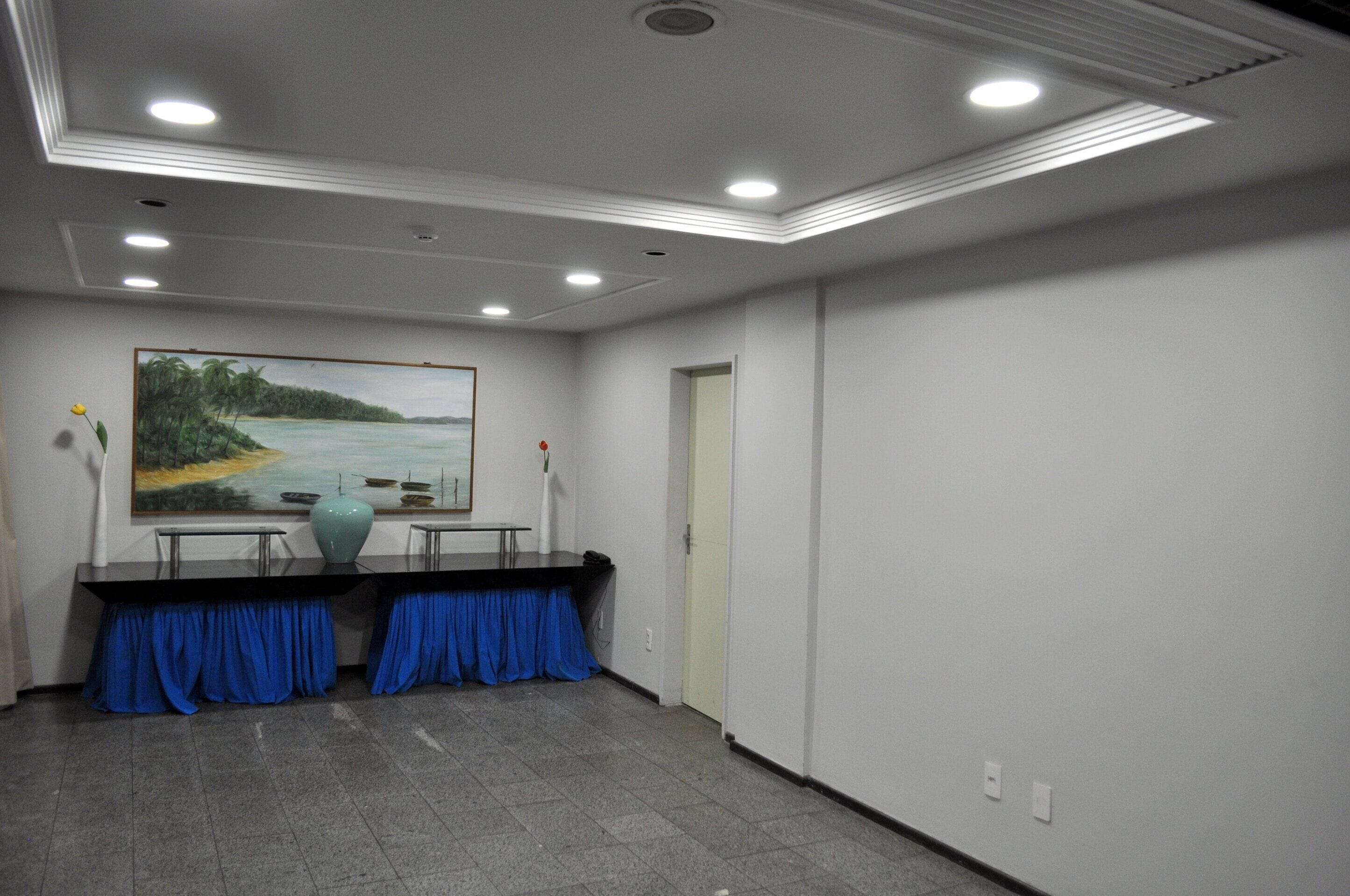 A conference room with a painting of a coastal landscape, a table with a vase, and blue curtains.
