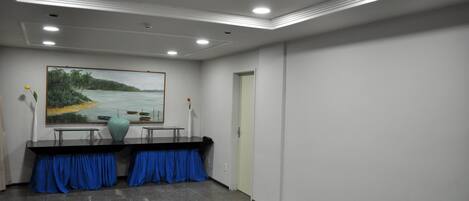 Un salón de conferencias con un cuadro de un paisaje costero, una mesa con un florero y cortinas azules.