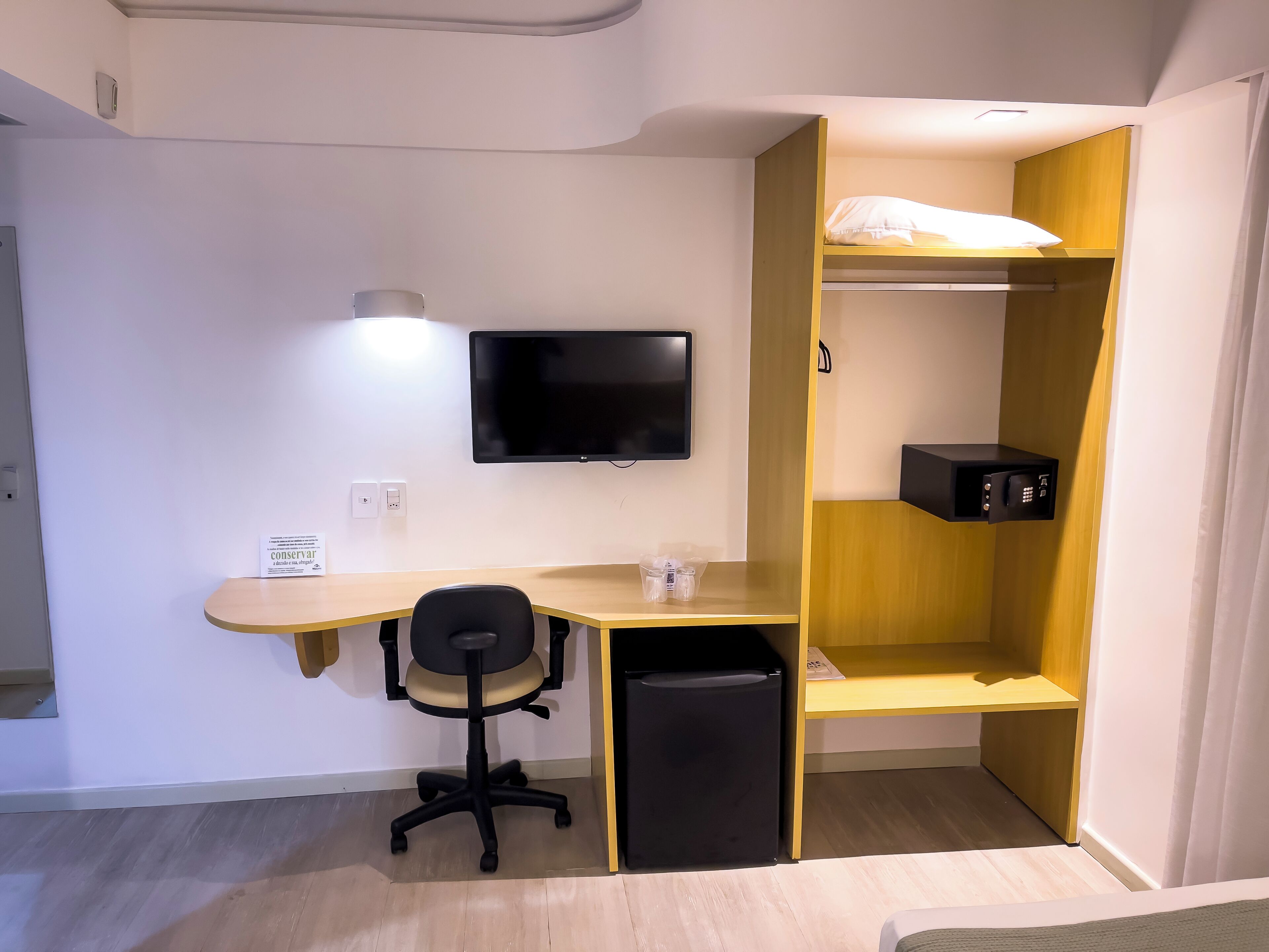 A compact room with a desk, chair, TV, and a small black trash bin.