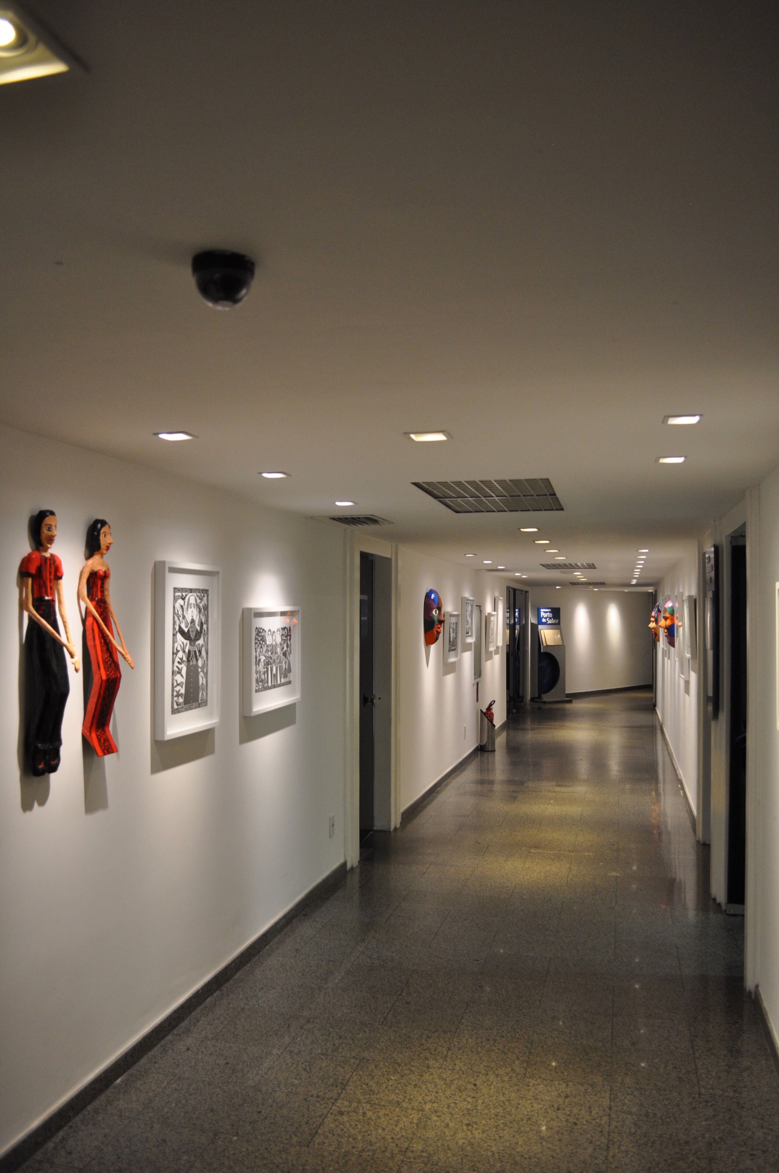 A hallway with art installations on the walls, a long corridor, and a ceiling with recessed lighting.